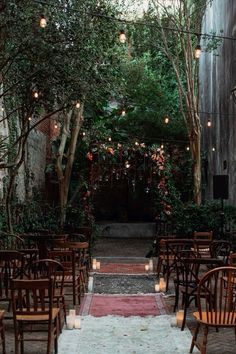 an outdoor ceremony setup with wooden chairs and candles on the aisle, surrounded by greenery