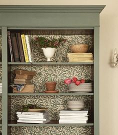 a green bookcase filled with lots of books next to a wallpapered wall