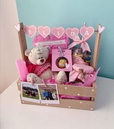 a teddy bear sitting in a wooden box with pink decorations and pictures on the table