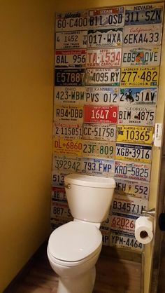 a white toilet sitting inside of a bathroom next to a wall covered in license plates