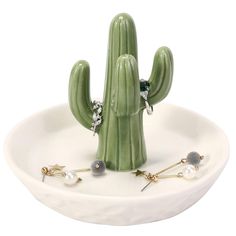 a green cactus with earrings on it sitting in front of a white bowl filled with other items