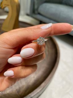 a woman's hand holding a diamond ring on top of her finger, in front of a couch