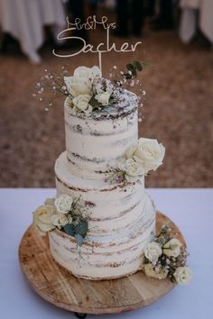 a three tiered cake with flowers on top is sitting on a wooden platter