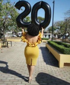 a woman in a yellow dress holding up large black numbers