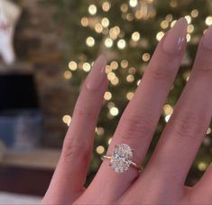 a woman's hand with a ring on it and a christmas tree in the background