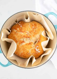 a loaf of bread sitting in a pot on top of a white tablecloth with blue handles