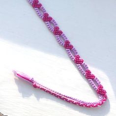 a pink and purple beaded necklace laying on top of a white surface next to a pair of scissors