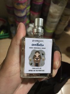 a person holding a small bottle of perfume in their left hand with the label on it