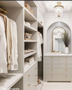 a walk - in closet with white cabinets and gold handles, an oval mirror on the wall