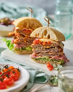 two sandwiches with meat, tomatoes and lettuce are on a white platter