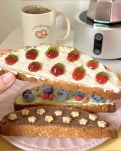 a person is holding two pieces of bread with fruit and cream on it, while the rest of the sandwich has been cut in half