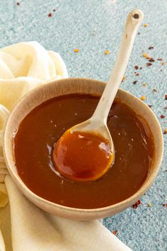 a spoon in a bowl filled with sauce on top of a cloth and napkins