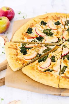 an apple and spinach pizza on a cutting board with sliced apples in the background