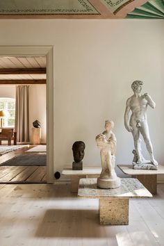 three statues are on pedestals in the middle of a room with white walls and wood floors