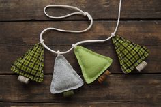 three green and white ornaments hanging from a string on a wooden surface, with two small pieces of fabric in the shape of trees