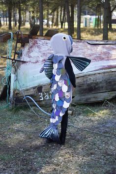 a paper fish that is standing in the grass next to an old boat with it's tail sticking out