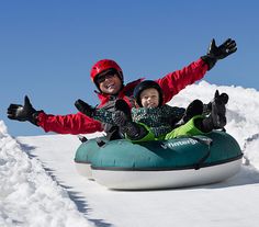 a man and child riding on an inflatable tube down a snow covered slope