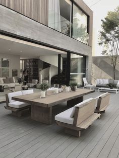 an outdoor dining table and benches on a wooden deck next to a large glass window