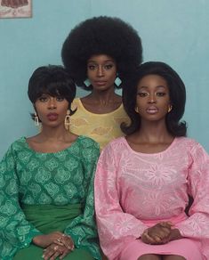 three women sitting next to each other in front of a blue wall with an afro hairstyle