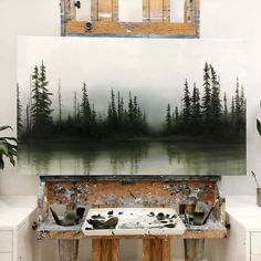 an artist's easel with paint and brushes on it in front of a painting