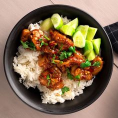 a black bowl filled with rice, meat and cucumber slices on top of it