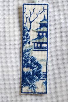 a blue and white bookmark hanging from a string on a piece of cloth with trees in the background