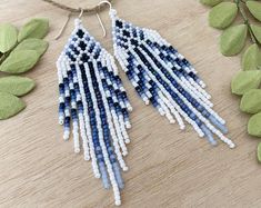 a pair of blue and white beaded earrings sitting on top of a wooden table