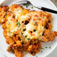 a white plate topped with lasagna covered in sauce and cheese next to a fork