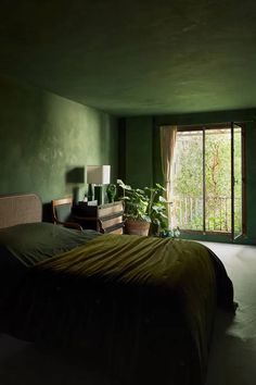 a bedroom with green walls and a bed in front of a window that looks out onto the woods