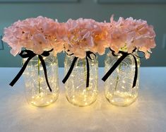 three mason jars with lights and flowers in them