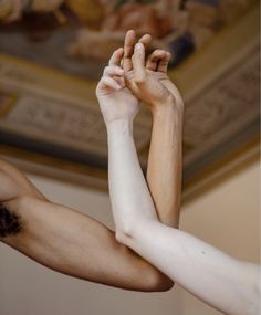 two hands reaching up towards each other in front of a ceiling with a painting on it