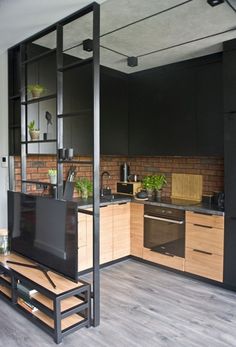 a kitchen with black cabinets and wooden flooring next to a tv on a stand