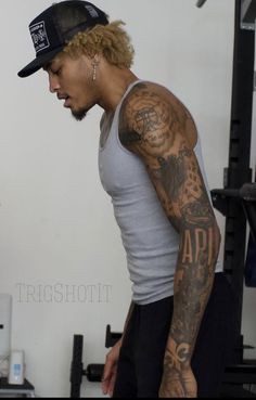 a man with tattoos on his arm standing in front of a gym equipment rack and looking down