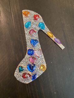 a painted letter made out of various colored stones on top of a wooden table next to scissors