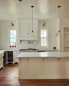 a large kitchen with white cabinets and wood flooring, along with an island in the middle