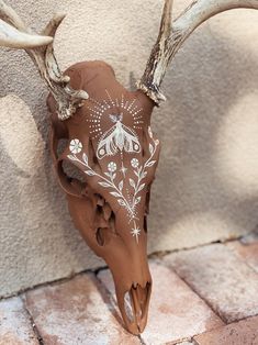 an animal skull with white flowers painted on it's antlers is sitting against a wall