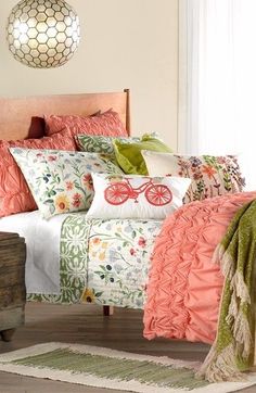 a bed covered in lots of pillows and blankets next to a wooden chest with drawers