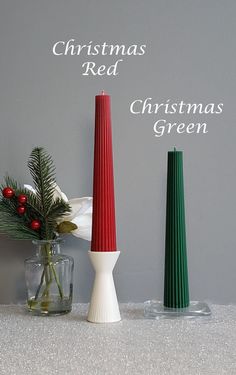 three christmas candles sitting on top of a table next to a vase filled with greenery