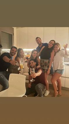 a group of people standing around each other in a kitchen holding wine glasses and posing for the camera