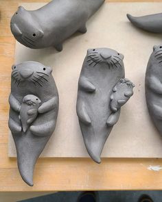 four clay animals are sitting on a wooden table and one is holding a baby seal