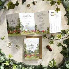 two wedding cards with trees and flowers on them, sitting next to each other in front of greenery