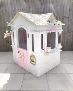 a doll house made out of white bricks with pink trimmings and flowers on the roof