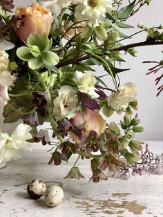 an arrangement of flowers and birds eggs on a table with white walls in the background