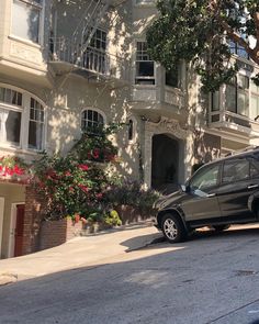 a black suv parked in front of a white building on a street corner with trees and flowers