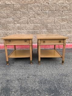 two wooden end tables sitting next to each other on the ground in front of a brick wall