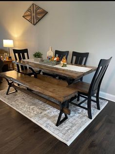 a dining room table with benches and chairs on top of a rug in front of a white wall