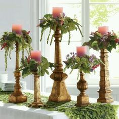 there are many candles that are on the table with flowers and greenery in them