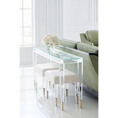 a glass table with two stools and flowers on it in front of a couch