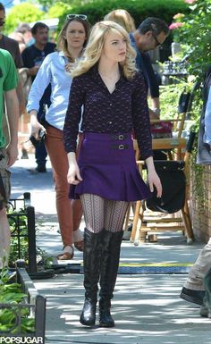 a woman in a purple dress and black boots is walking down the street with other people