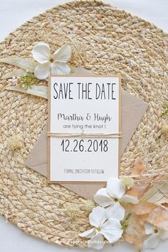 save the date card on top of a straw mat with flowers and leaves around it